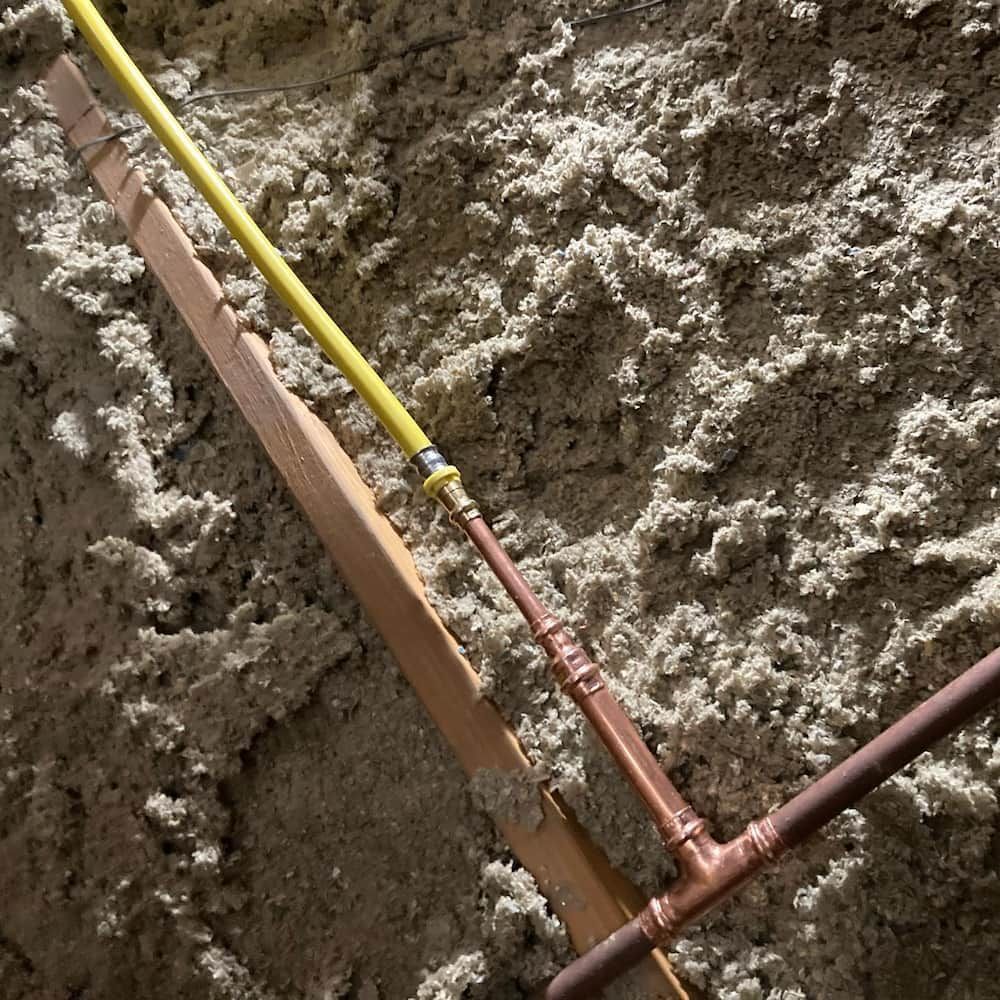 Copper Pipes and Yellow Conduit Secured to a Wooden Plank — Corrimal Plumbing Services in Thirroul, NSW