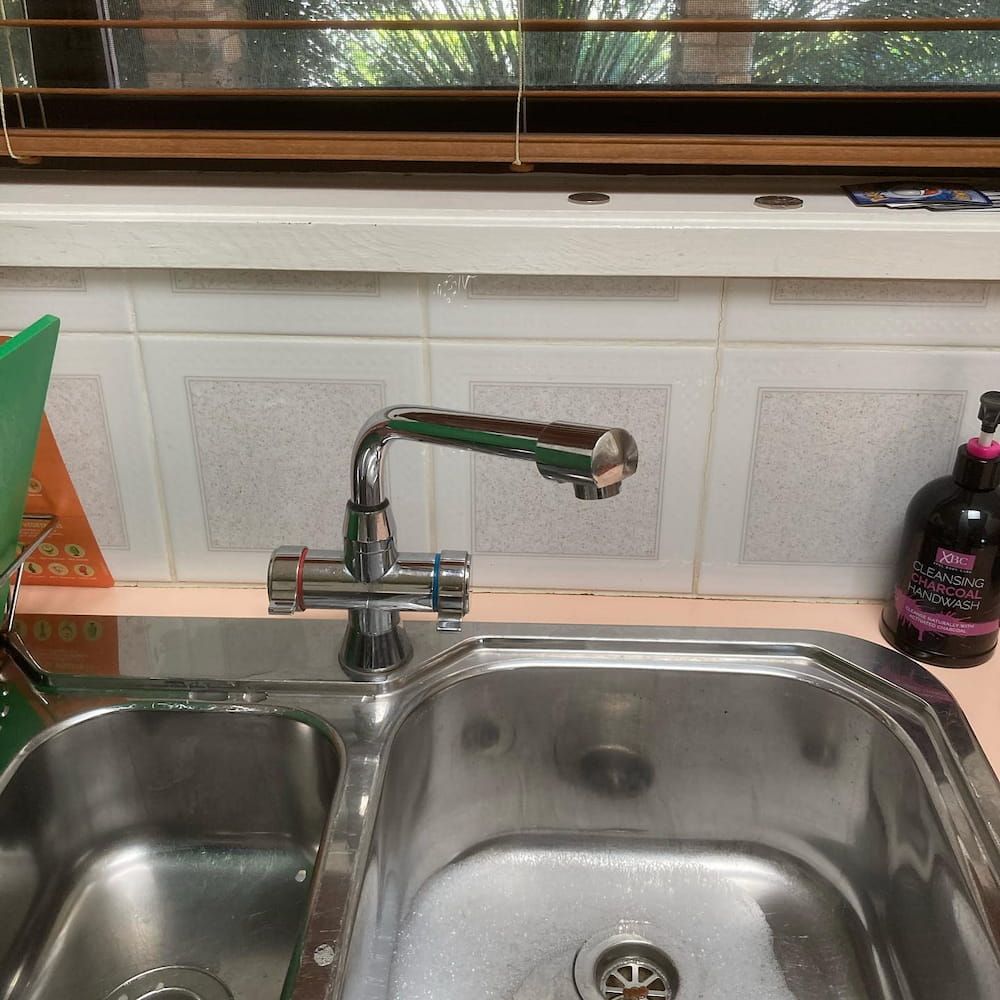 Stainless Steel Kitchen Sink With Faucet, Window Above, Soap Bottle — Corrimal Plumbing Services in East Corrimal, NSW