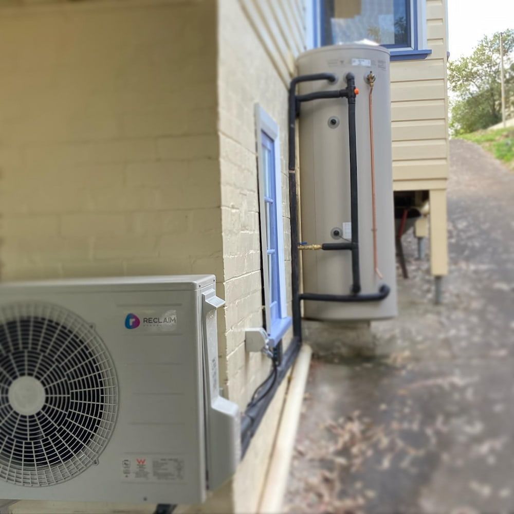 An Outdoor Heat Pump Unit and a Water Heater Installed on a Building's Exterior — Corrimal Plumbing Services in Bulli, NSW