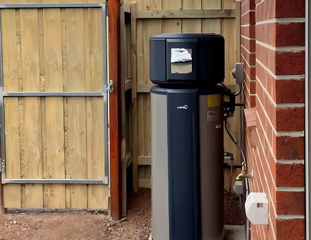 Water Heater Next to a Brick Wall and Wooden Fence — Corrimal Plumbing Services in Woonona, NSW