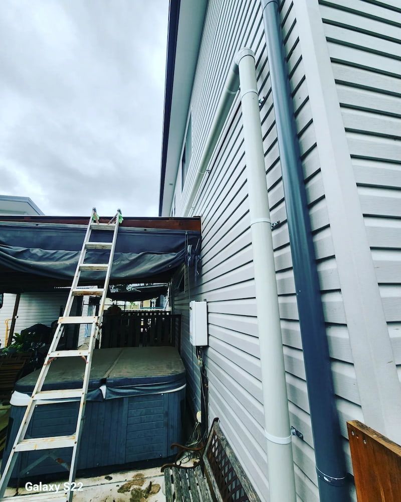 Side of a House With White Siding and a Downspout, Ladder, and Hot Tub — Corrimal Plumbing Services in East Corrimal, NSW