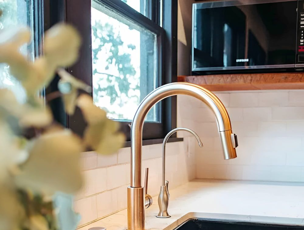 Gold Kitchen Faucet Over a Black Sink With a Window Backdrop — Corrimal Plumbing Services in Thirroul, NSW